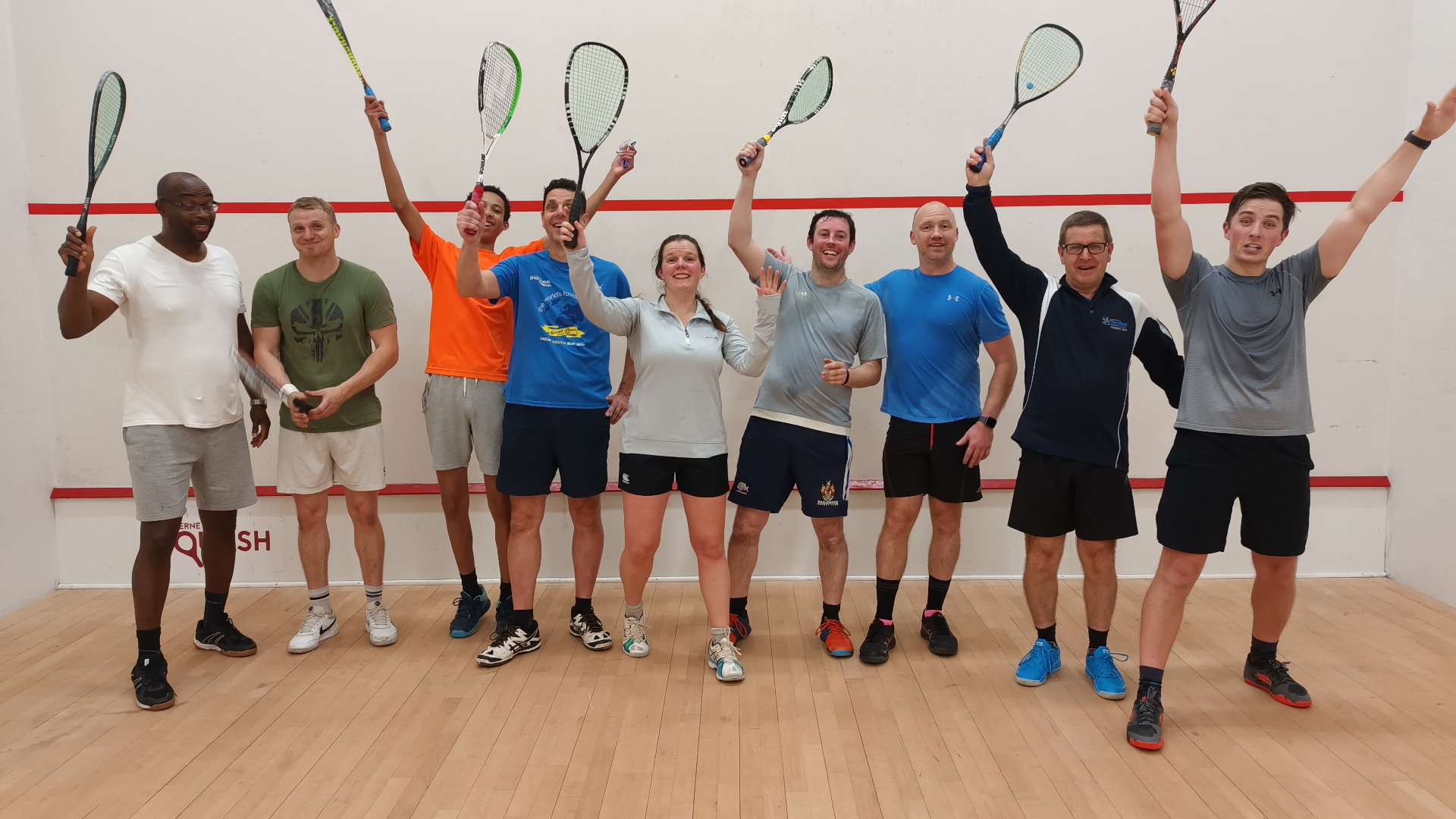A cheerful group of squash players raising their rackets on court